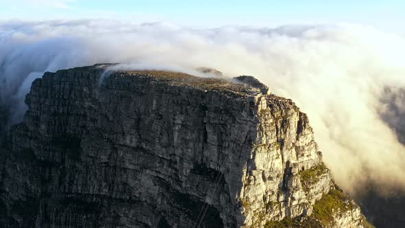 Aerial footage of a large bank of clouds roll over the side of Table Mountain