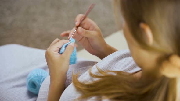 Pregnant Woman Sits At Home On Sofa And Knits From Yarn alt