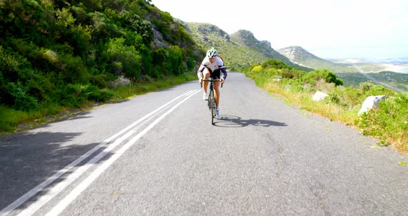 Female cyclist cycling on a countryside road beside a lush mountain  alt