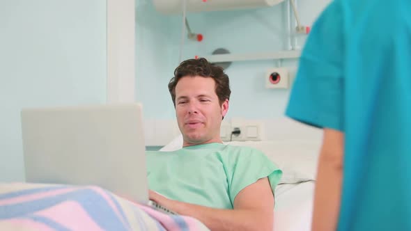 Happy male patient typing on a laptop while lying on a bed alt