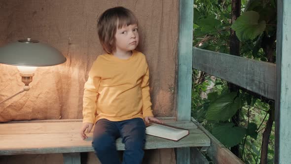 Cute Little Girl on the Porch of a Village House is Trying to Read a Book