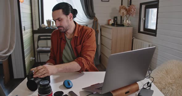 A Young Handsome Male Photographer and Videographer Works at Home on a Laptop alt