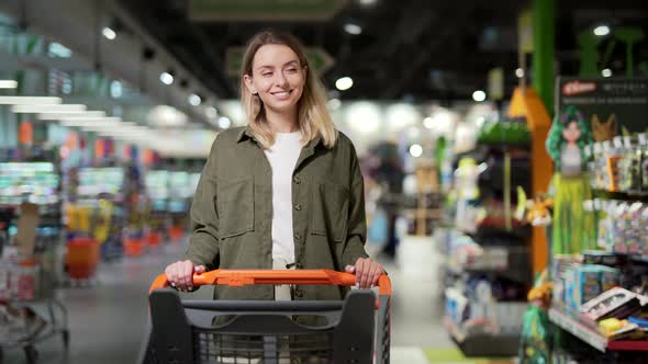 young happy woman pushing trolley spends time in a supermarket or mall store. alt