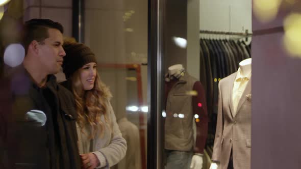 Man and woman stop to look at clothes while widow shopping alt