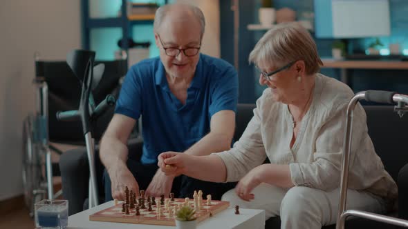 Elder Couple with Disability Playing Chess Game on Board at Home alt
