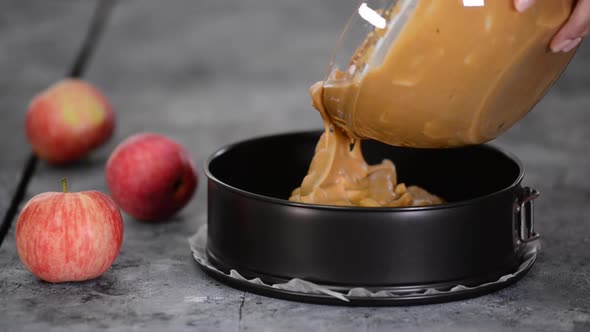 Female chef hands pouring batter into baking dish for apple pie.