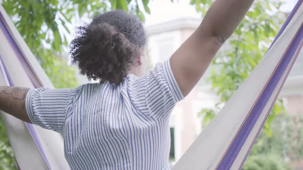 Back View of Young African American Woman Sitting in the Hammock, Relaxing in the Backyard alt