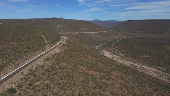 Desert Road Across Arid Mountain Terrain with Bush and Cactus