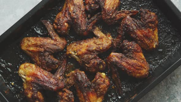 Grilled Chicken Wings in Spices in Black Metal Baking Tray on Stone Table. Top View alt