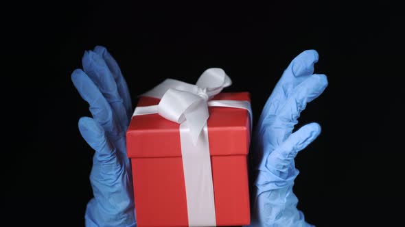 Person's Hands in Blue Protective Gloves Holding Red Gift Box with White Ribbon