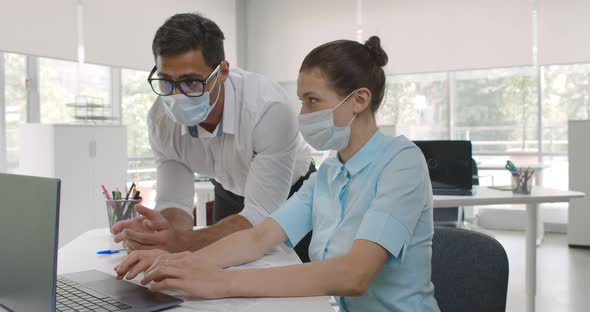 Diverse Male and Female Business Colleagues in Face Mask Discuss Using Laptop in Office alt