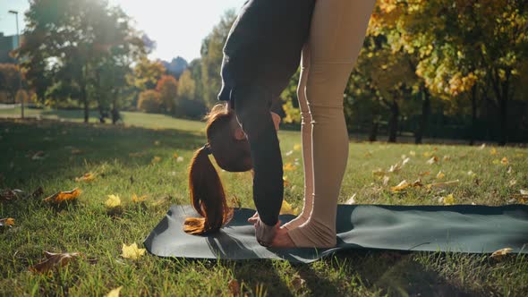 Young Woman Practices Standing Fold Yoga Pose in Autumn City Park on a Mat