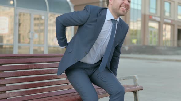 Businessman having Back Pain while Sitting on Bench Outdoor alt