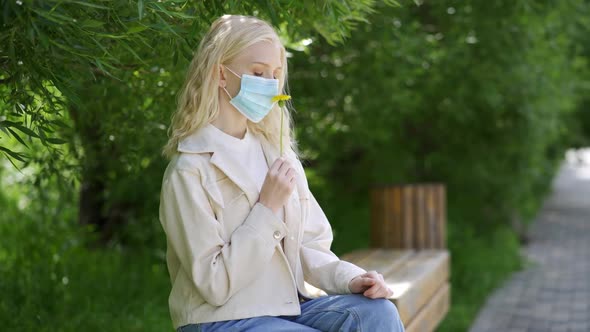 Young Beautiful Woman in a Medical Mask Sniffs a Yellow Flower