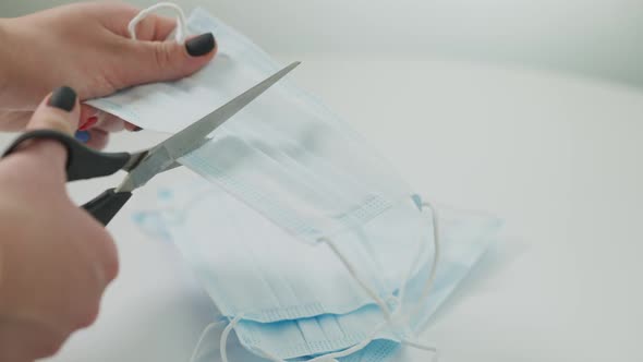 Female Hands Cutting Coronavirus Face Mask with Scissors alt