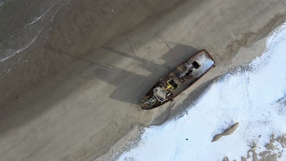 Aerial Top View of Old Wrecked Fishing Ships Drowned at the Sea Shore in Snowy Winter Season alt
