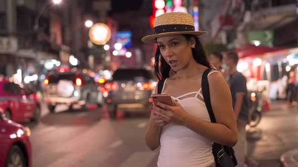 Young Brunette Woman Using a Mobile Phone Hail a Taxi at Night on Downtown Street alt