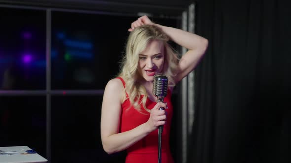 Seductive Blond Caucasian Woman with Blue Eyes in Red Dress Singing with Microphone on Stage alt