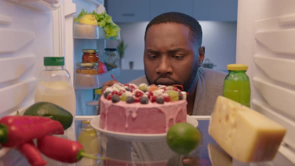 Sleepy man eating cake at night. View from inside fridge