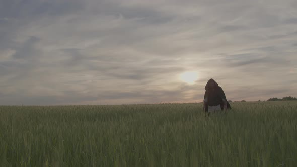 Man in Medieval Clothes Walks Through Wheatfield at Sunset Touching Wheat Ears