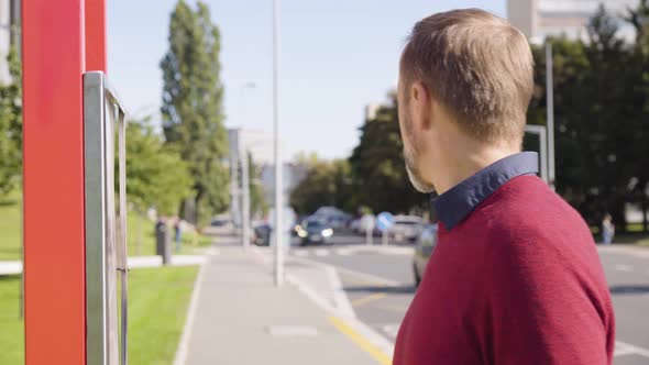 A Middleaged Handsome Caucasian Man Reads a Bus Schedule at a Bus Stop in a Street alt