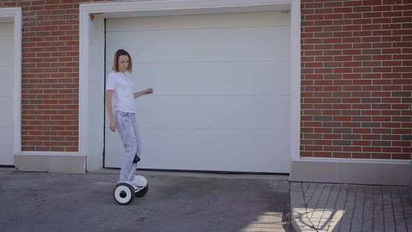 A Slender Young Girl Rides a Gyro Scooter Along a City Street. Modern Electric Transport. alt