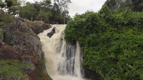 Drone shot flying up over a water fall in the Jungle of Africa with people on-top of the waterfall. alt