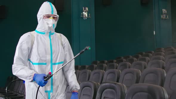 Worker in Antivirus Uniform Spraying Disinfectant at Cinema alt
