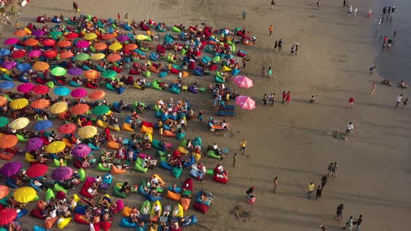 tourists relaxing on the multicolored beanbags under colorful umbrellas on the tropical sandy beach. alt