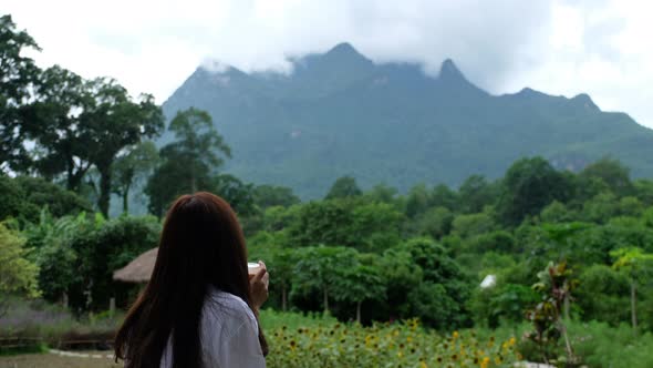 A young asian woman drinking coffee and looking at a beautiful mountain on foggy day