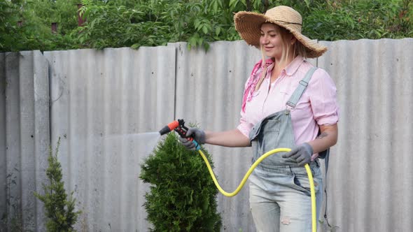 A Young Adult Woman Wateres a Vegetable Garden with a Garden Hose Outside the House alt