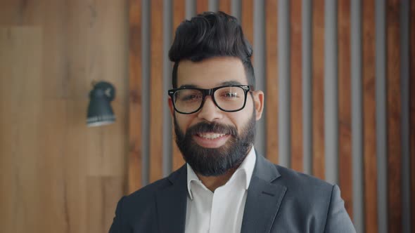 Portrait of Handsome Middle Eastern Man Wearing Glasses and Suit Standing Indoors Smiling alt