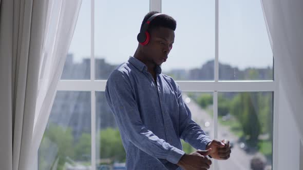 Middle Shot of Joyful Young Man in Headphones Dancing and Singing at Window in Home Office alt
