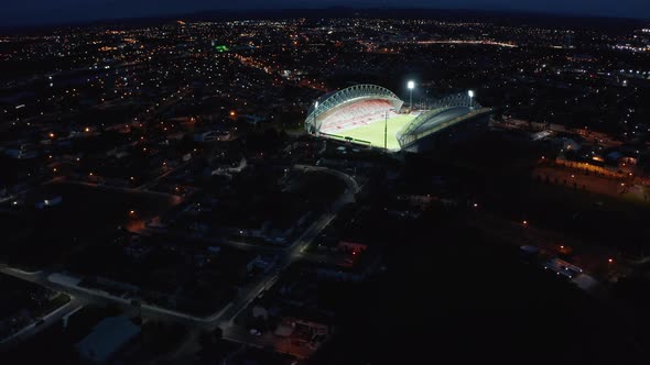 Descending Panoramic Footage of Night City with Glowing Illuminated Football Stadium alt