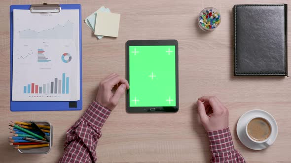 Top View of Male Hands Scrolling on the Left Edge of a Green Screen on a Black Tablet alt