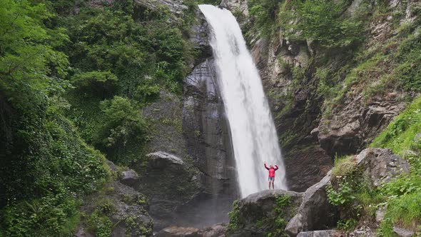 Hiking Woman in Red Jacket Dancing Near Big Waterfall