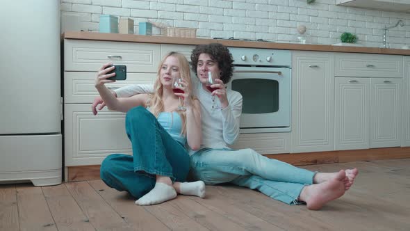 Young Couple Taking Selfie on Smartphone Sitting on the Floor of the Kitchen Background alt