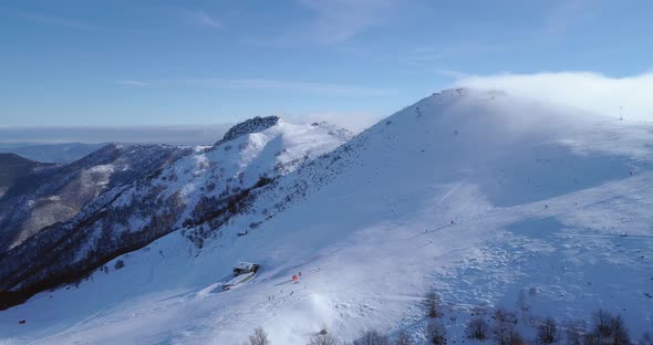 Backward Aerial Over Winter Snowy Mountain Top Ski Tracks Resort with Skier People Skiing