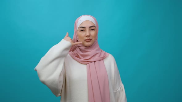Young Muslim Woman in Hijab Pointing Index Finger on Camera Doing Phone Gesture Like Says Call Me