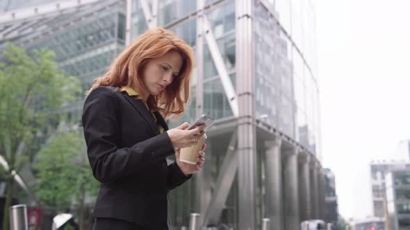 Businesswoman in city using smart phone with takeaway coffee