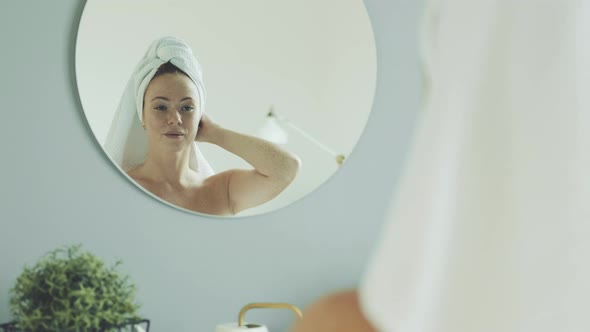 Happy attractive woman looks in bathroom mirror in morning