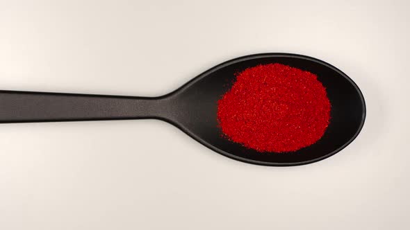 Red pepper powder fill a plastic spoon on a table