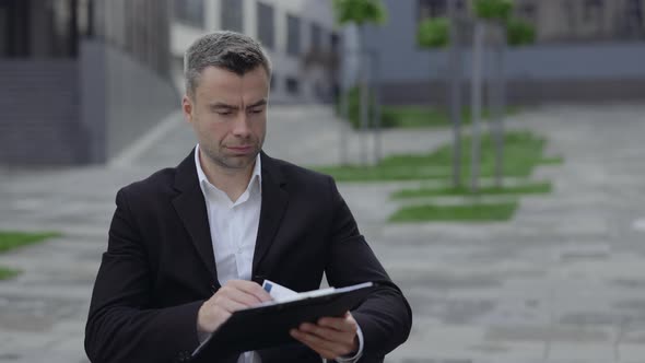 Close Up View of Successful Man in Wheel Chair Looking Through Documents at City Street alt