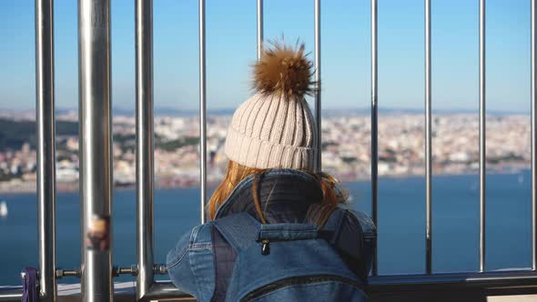 Woman Traveler with Long Hair Under Winter Hat Stands at Cristo Rei Statue Deck alt