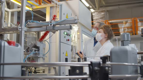 Operators in Safety Mask and Lab Coat Controlling Production Line From Control Panel alt