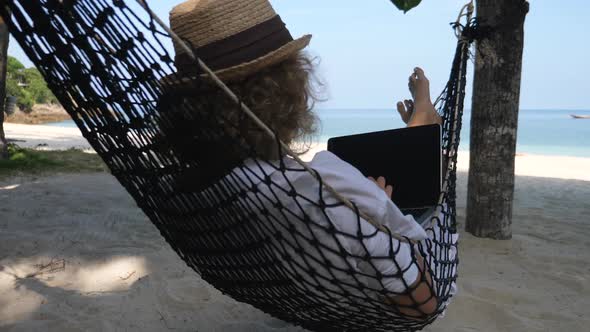 Businesswoman Working With Laptop Lying In Hammock On The Beach alt