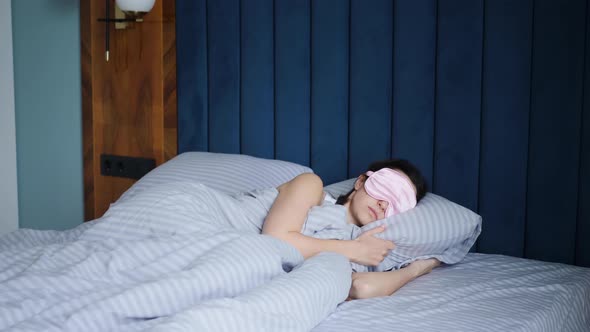 Woman in a Pink Eye Mask Lies Under a Blanket in a Bed and Suffers From Insomnia alt