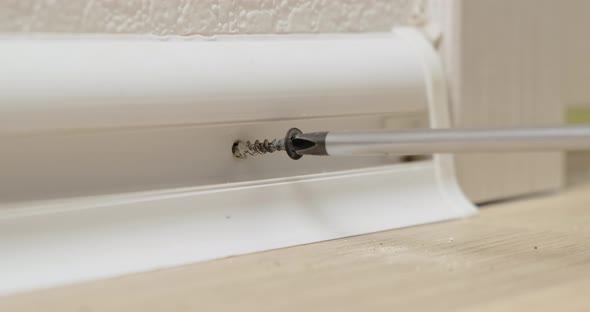 Professional man work on the installation of plastic plinth on white wall. Close up. alt