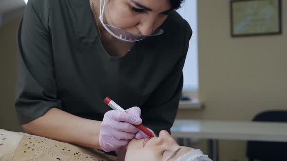 A Permanent Makeup Artist Draws a Contour Sketch of Future Lips with a Red Cosmetic Pencil