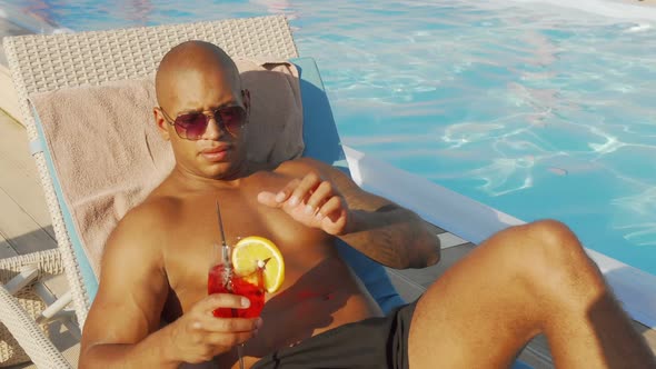 Handsome African Man Drinking Cocktail Sunbathing at the Poolside